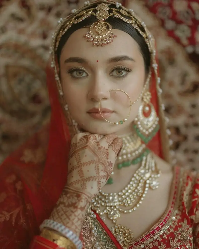 Close-up of a bride resting her chin on her hennaed hand, wearing a maang tikka and kundan jewellery