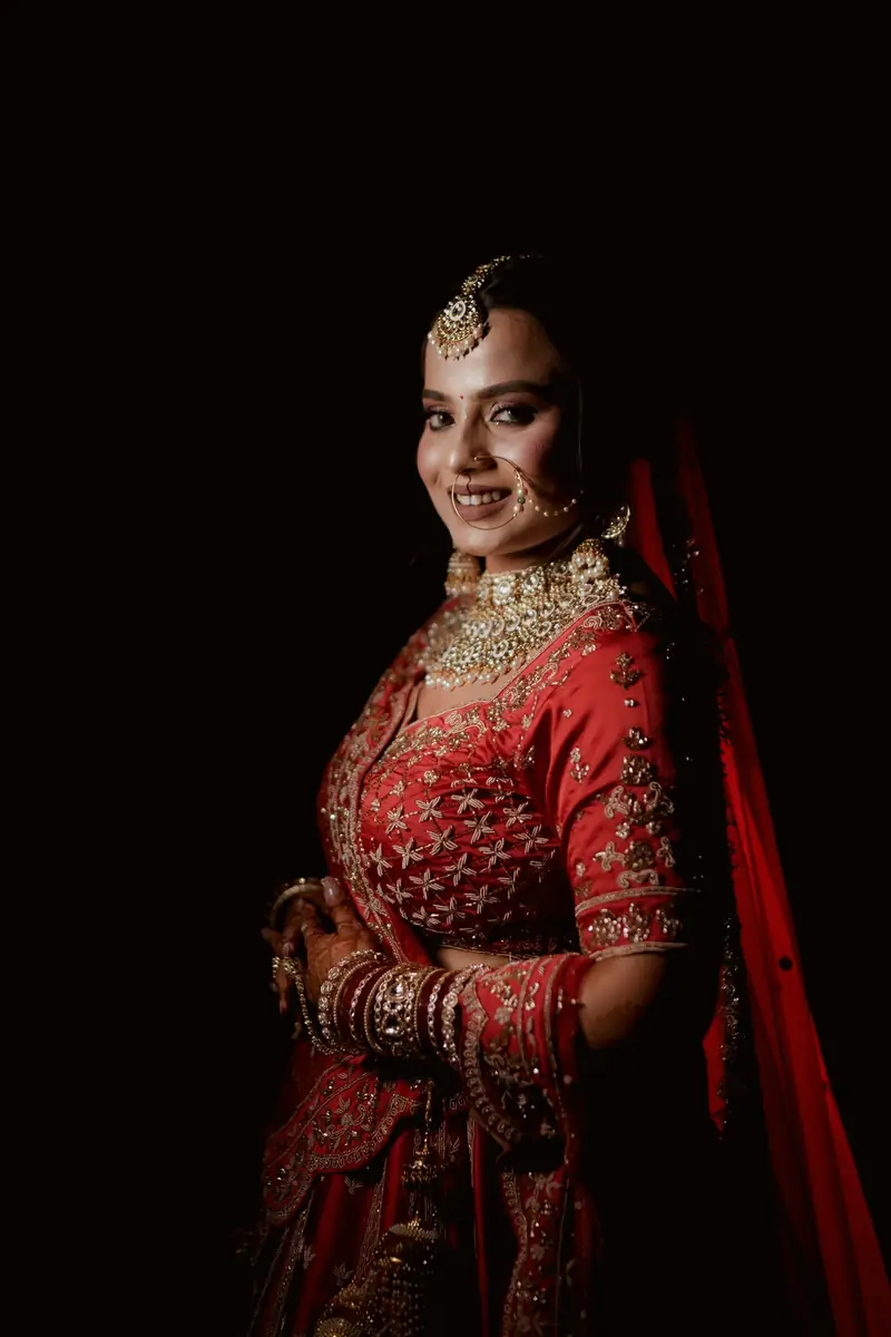 A bride in a red lehenga lit softly against a dark background