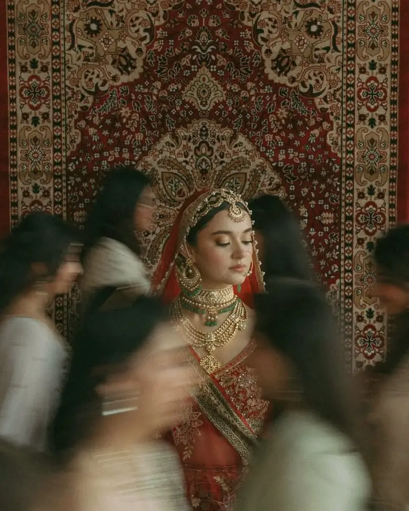 A bride standing still against an antique rug as her friends rush past in a blur