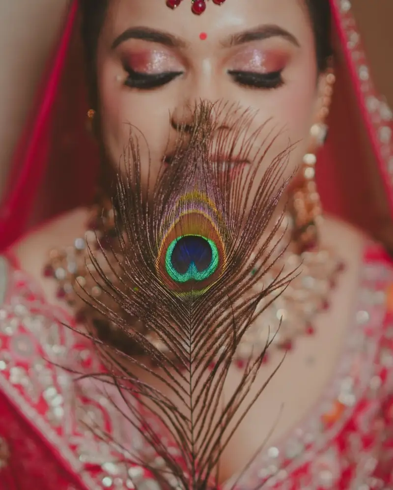 A bride holding a peacock feather across her face, only her eyes showing