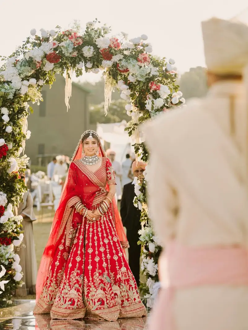 The bride walking towards the groom beneath a floral arch