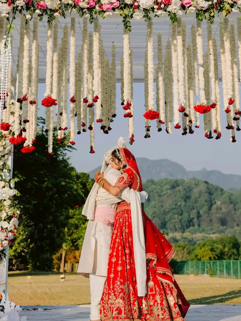 The couple embracing under hanging flowers with green hills behind them
