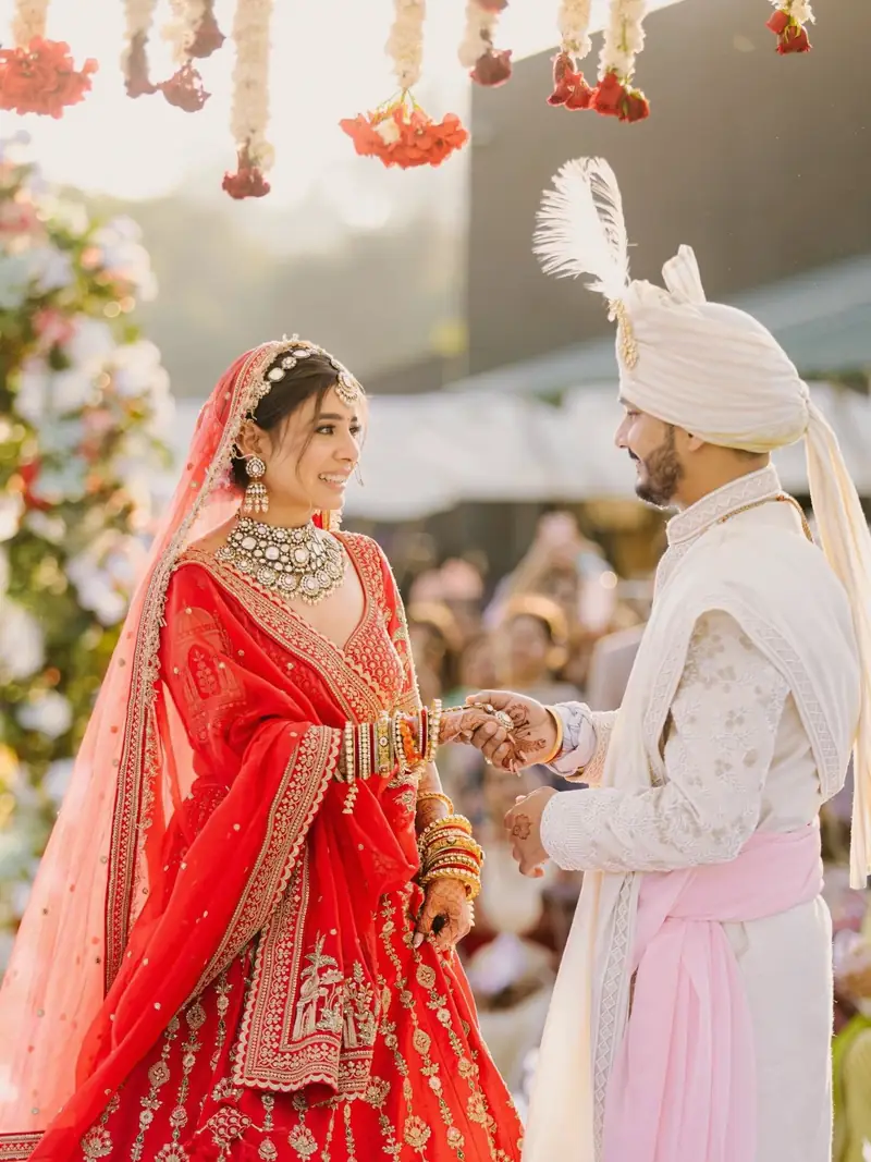 The bride in a red lehenga holding the groom's hands and laughing