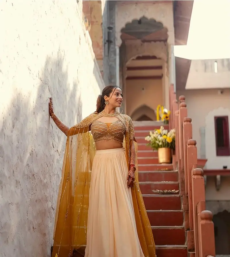 The bride posing on a stone staircase in a mustard and ivory lehenga
