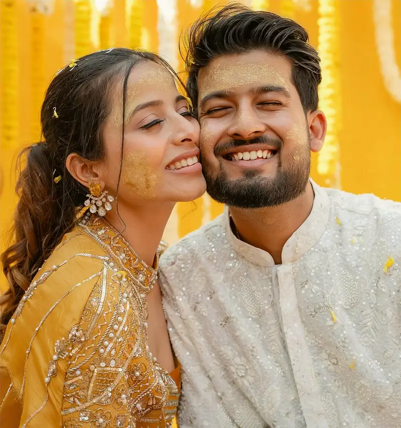 The couple cheek to cheek and laughing, her hands covered in mehendi