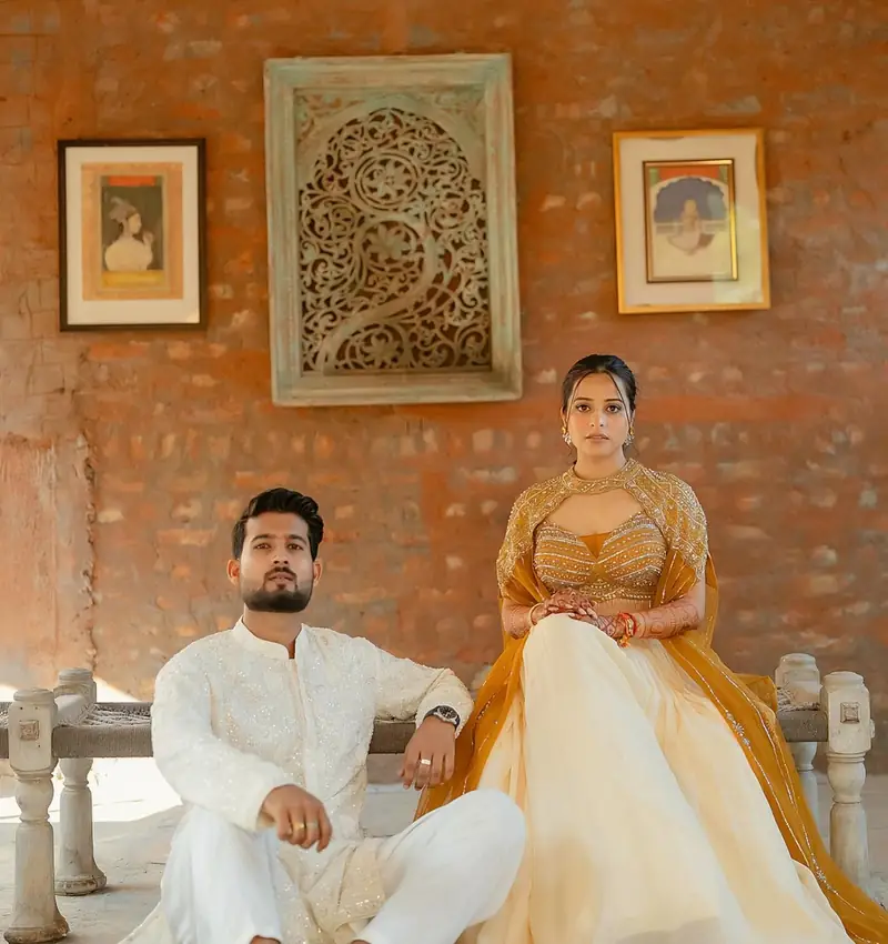 The couple seated side by side in a haveli, she in ivory and mustard, he in white