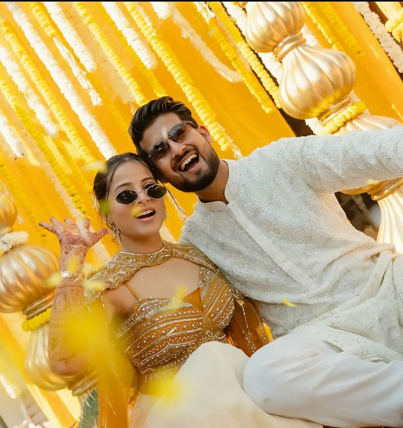 The couple in sunglasses posing playfully beneath yellow drapes and brass pots