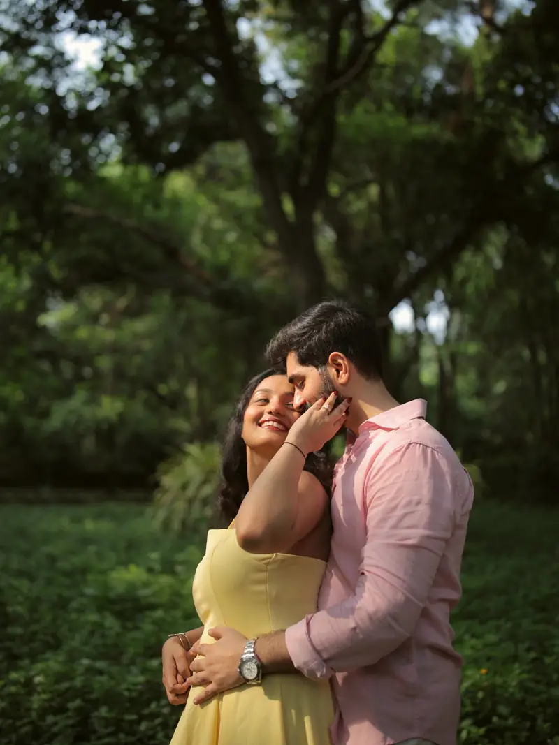 The couple embracing among the trees of Lodhi Garden, she in a yellow dress and he in a pink shirt