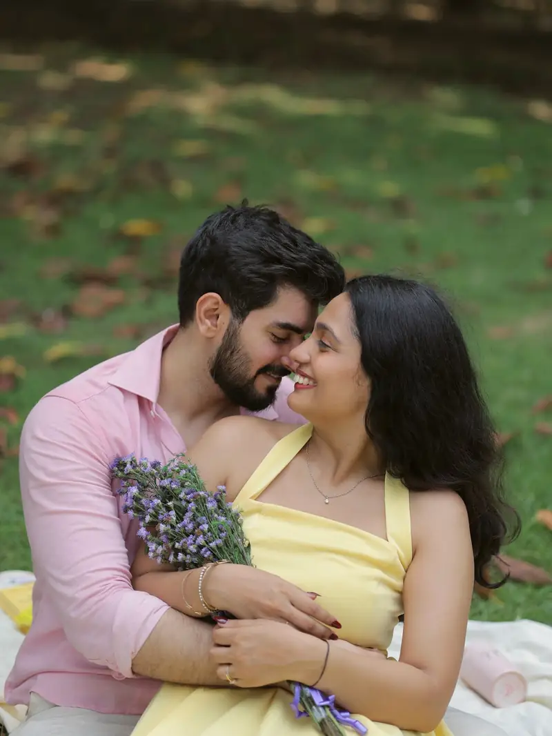 The couple sitting close on a picnic blanket, she holding a bouquet of lavender