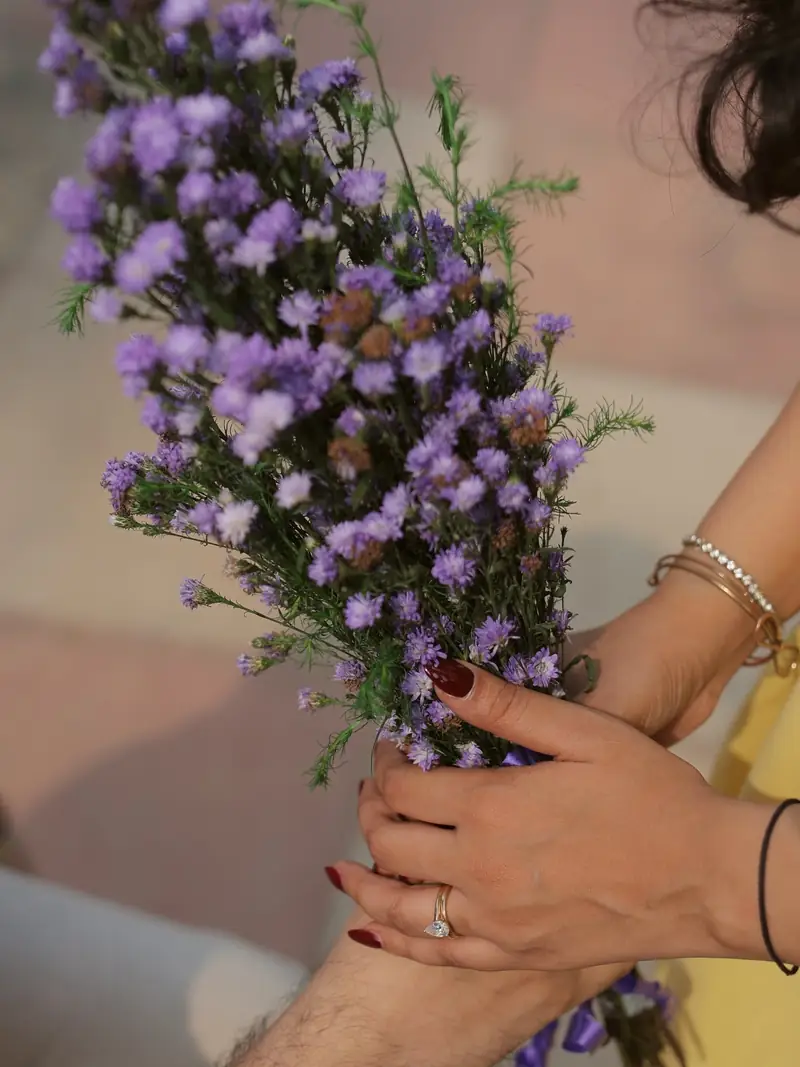 Close-up of her hand with an engagement ring resting on his arm, lavender in the background