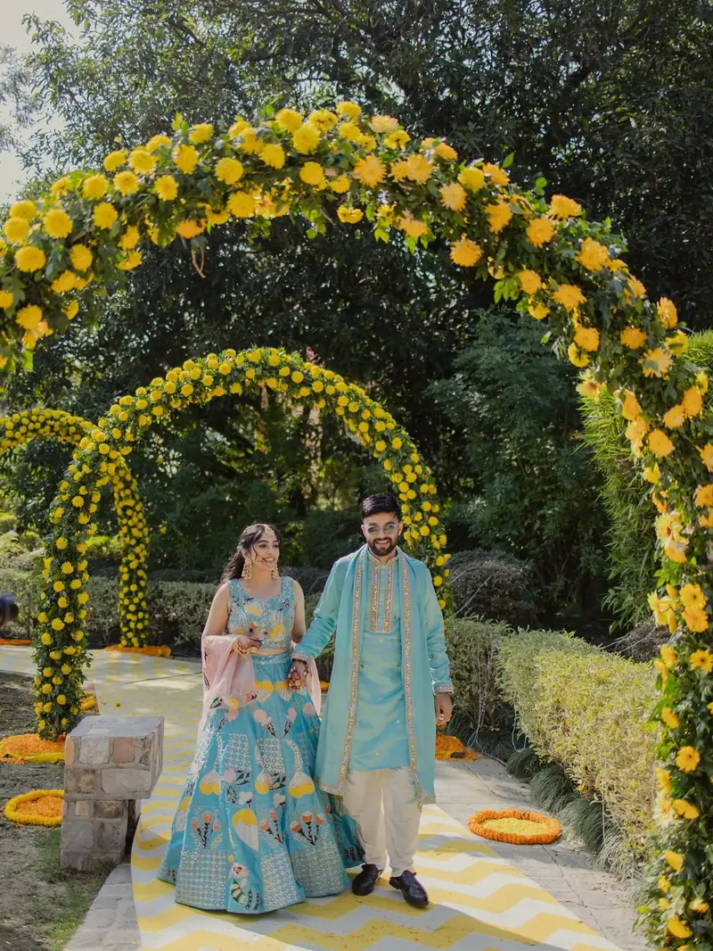 The couple walking hand in hand beneath arches of yellow marigolds
