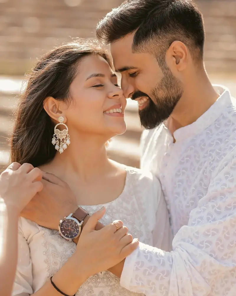 A couple laughing with their faces close together, both dressed in white