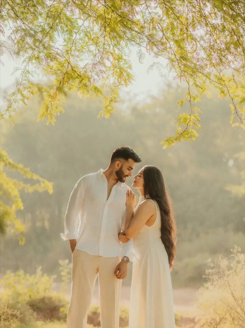 A couple dressed in white standing close under a tree in hazy golden light