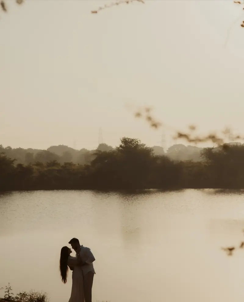 Silhouette of a couple kissing on a ledge above a lake at sunset