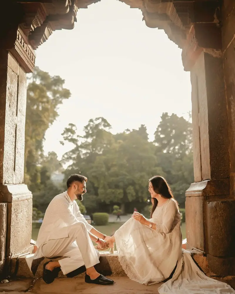 A couple sitting inside a carved stone archway with trees glowing behind them