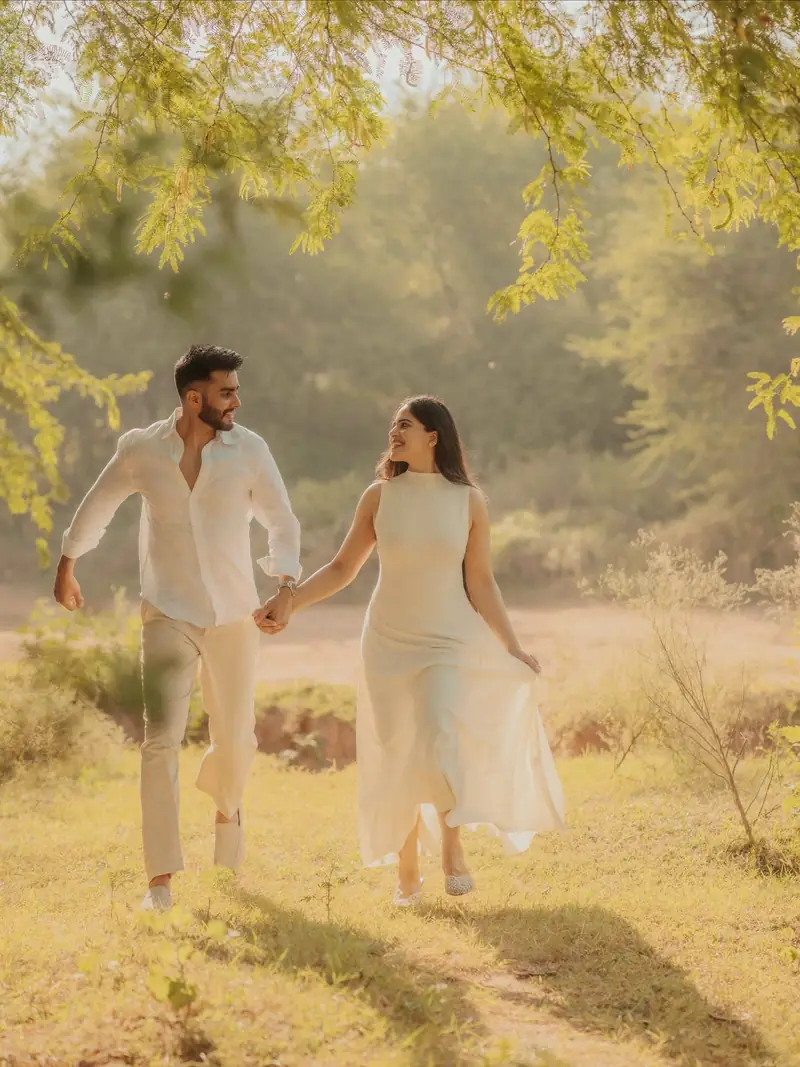 A couple walking hand in hand across a sunlit field of dry grass