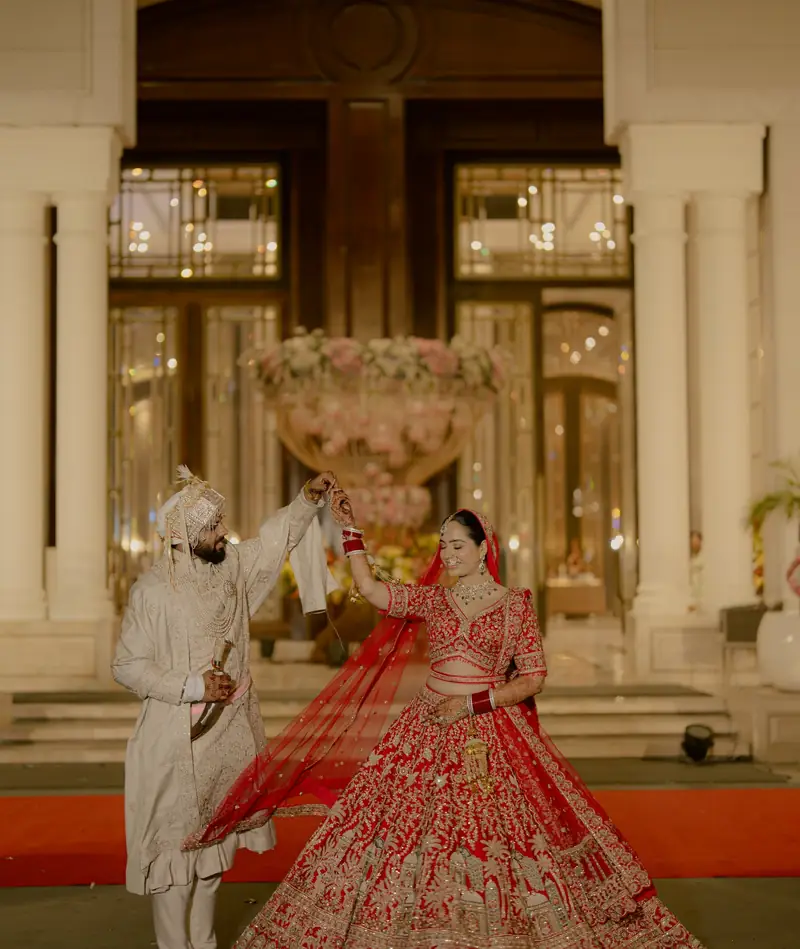 The bride swirling her red dupatta on the red carpet as the groom watches