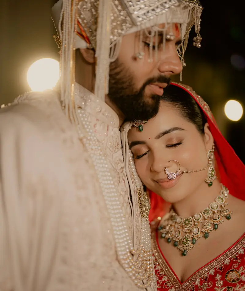 The bride resting her head on the groom's chest, eyes closed, his sehra beside her face