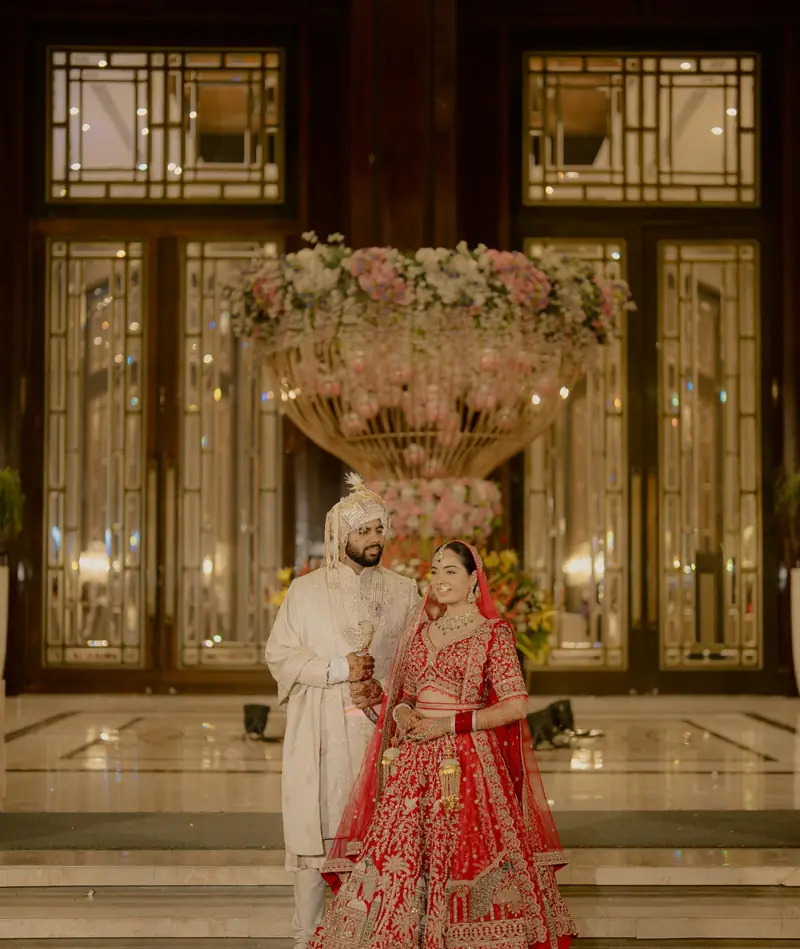 The couple standing on marble steps in front of tall glass doors and a giant floral urn
