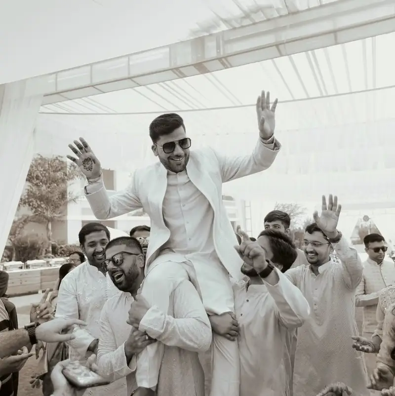 Black and white photo of the groom lifted onto his friends' shoulders during the baraat