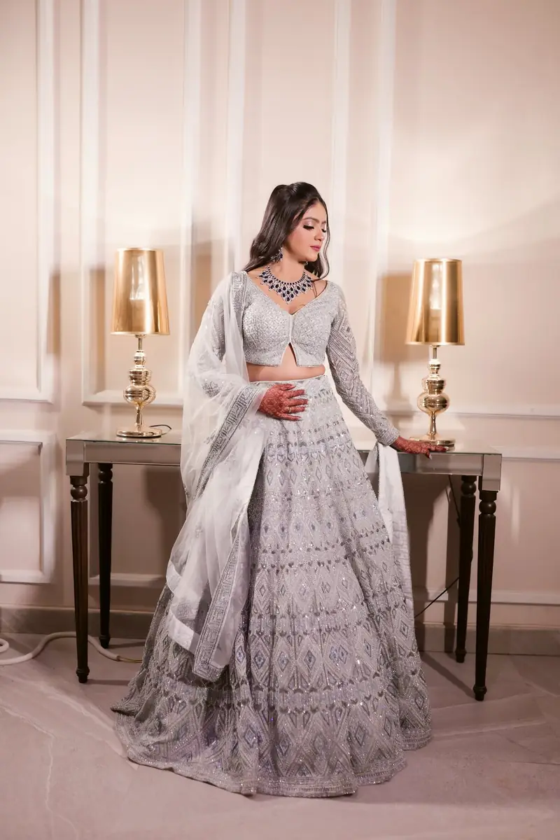 A bride in a grey embellished lehenga posing between two table lamps