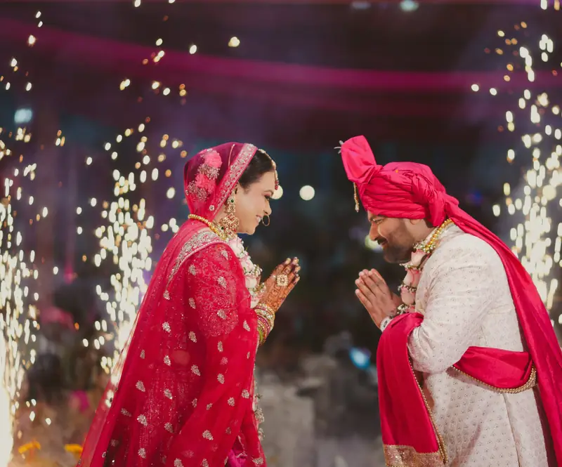 The bride and groom greeting each other with folded hands between sparkler fountains