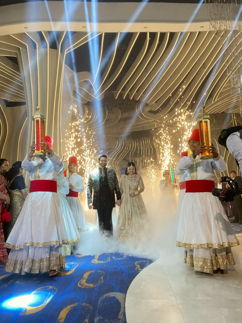 A couple's grand entry flanked by performers in white, with light beams and smoke