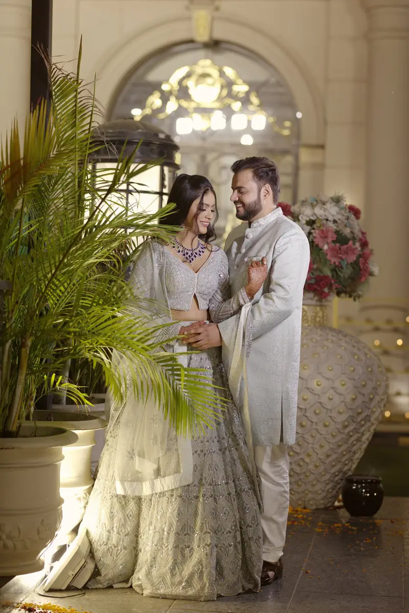 A couple in ivory and silver outfits embracing in a white palace-style hall
