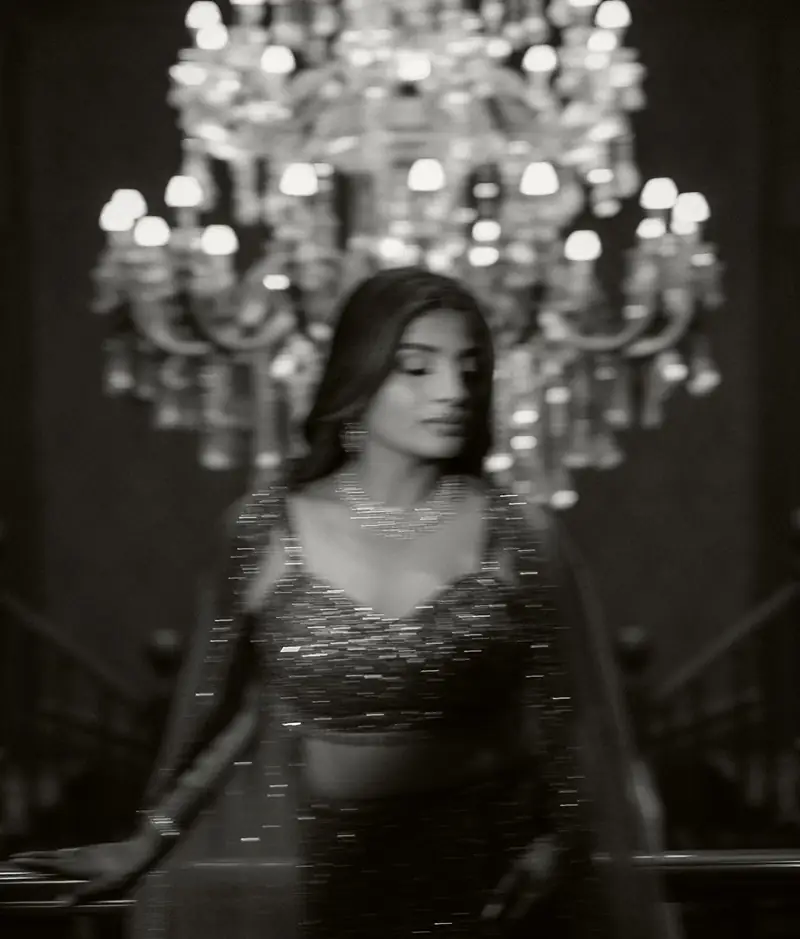 Black and white portrait of the bride standing before a glowing chandelier