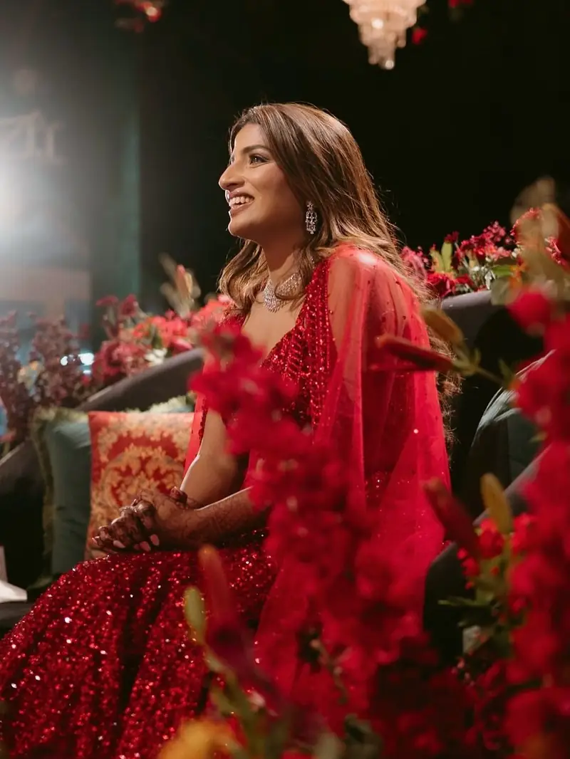 A bride in a red sequinned lehenga laughing, framed by red flowers