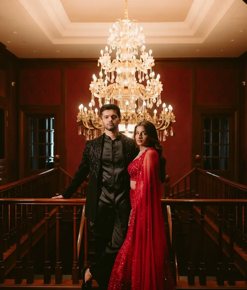 The couple posing on a wooden staircase landing beneath a crystal chandelier