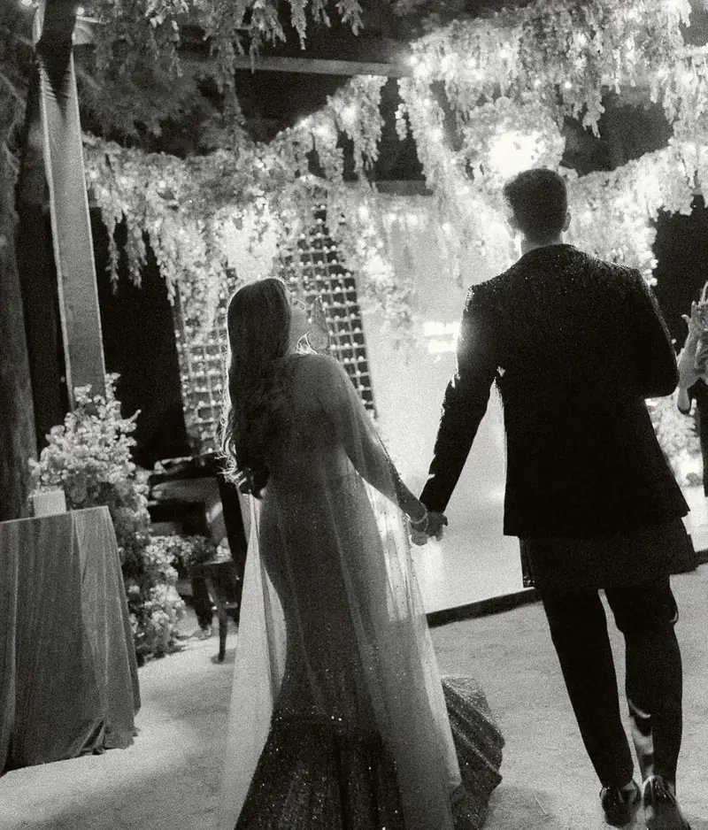 Black and white photo of the couple walking hand in hand under a canopy of hanging flowers