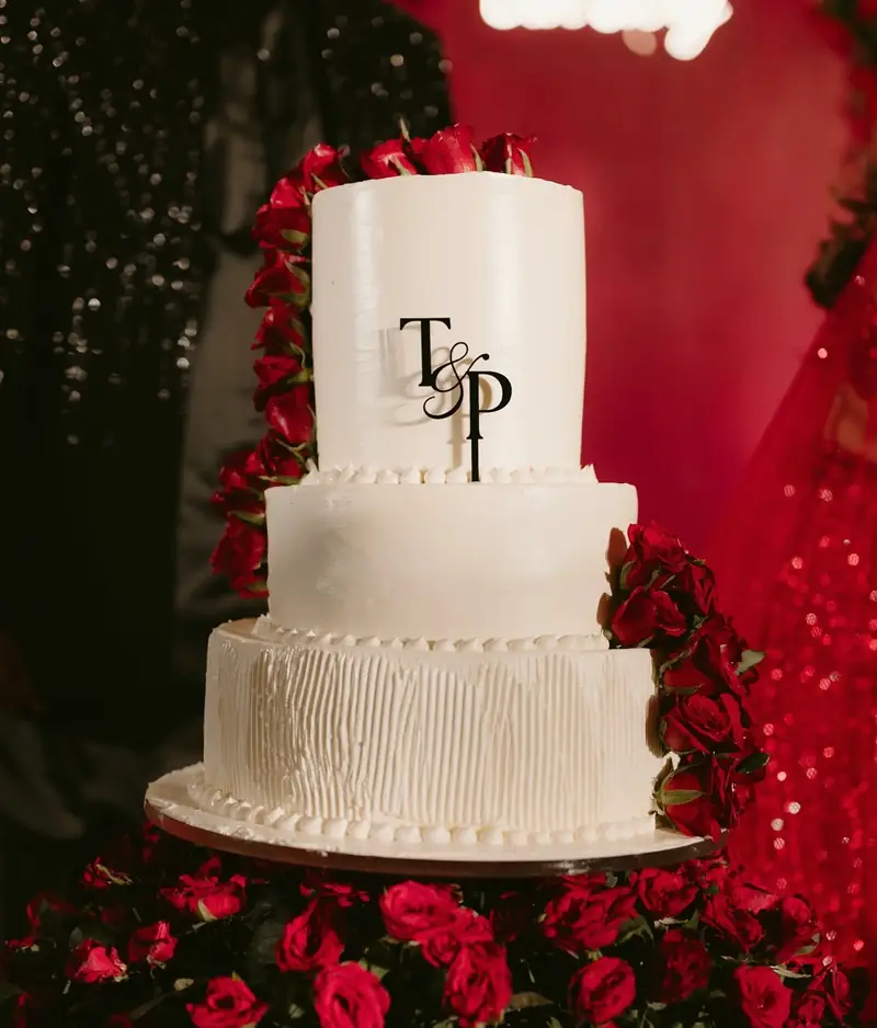 A three-tier white cake topped with the couple's initials and surrounded by red roses
