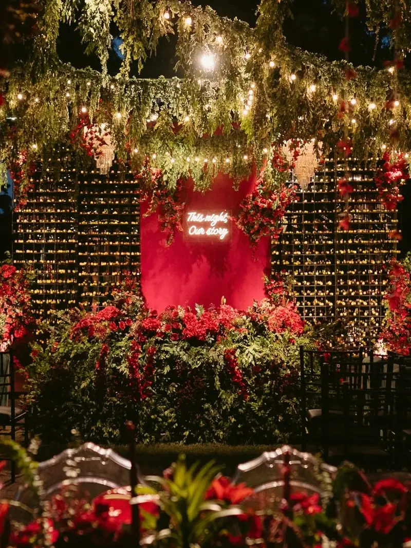 The sangeet stage dressed in red roses, hanging greenery and string lights
