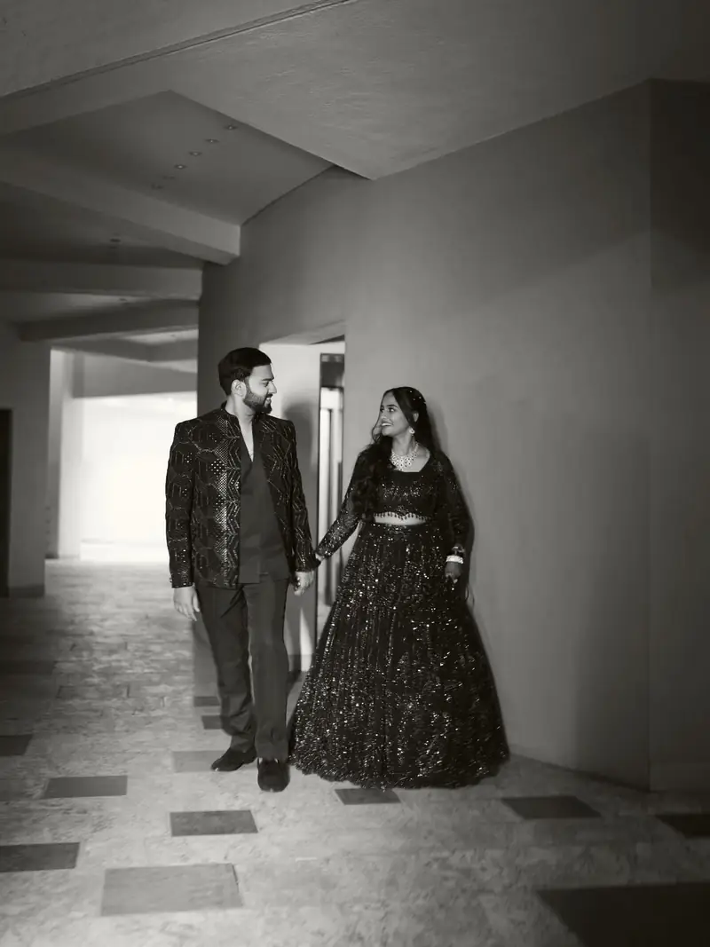 Black and white photo of the couple standing hand in hand in a long corridor