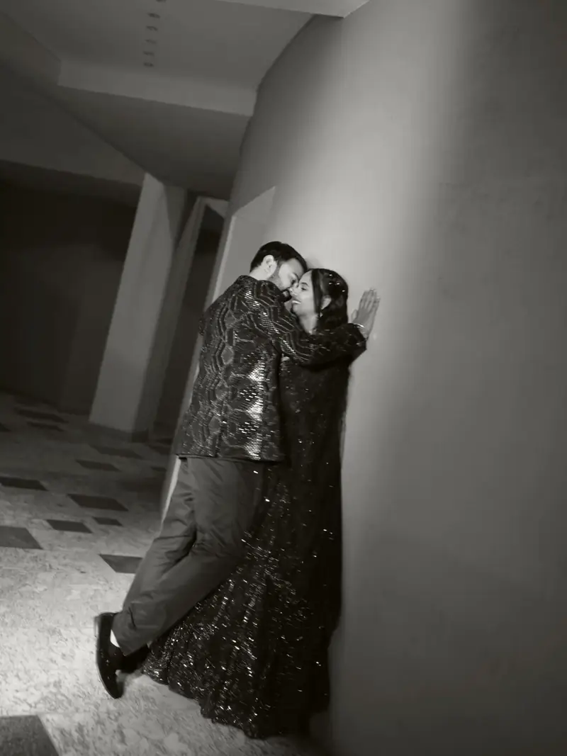 Black and white photo of the groom kissing the bride against a curved wall