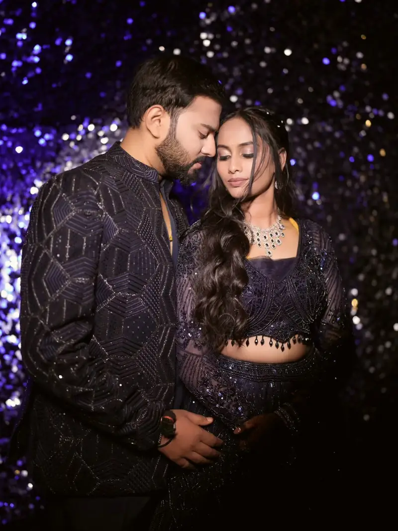 The couple in matching navy sequinned outfits in front of a glittering purple wall