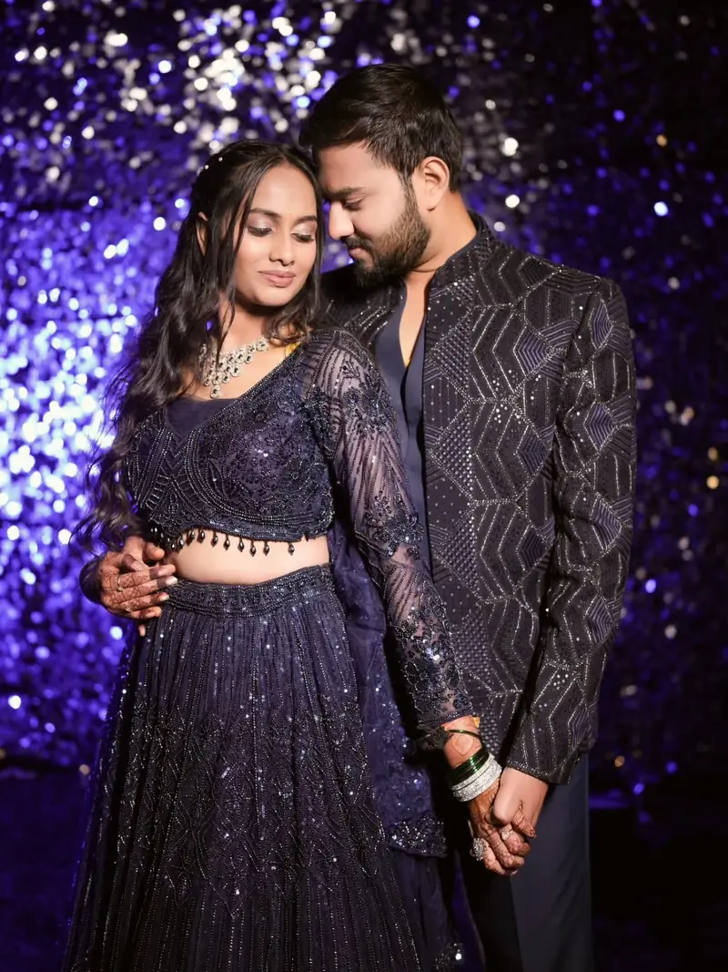 The couple holding each other and smiling in front of a sparkling purple backdrop
