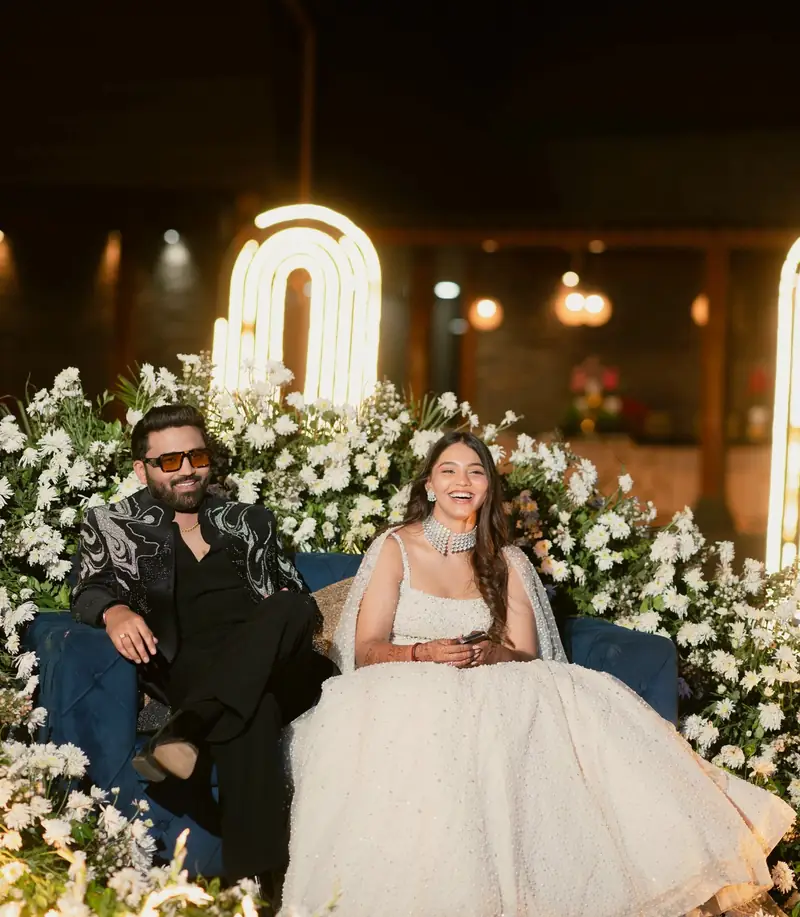 The couple seated on their flower-covered stage with warm lights glowing behind