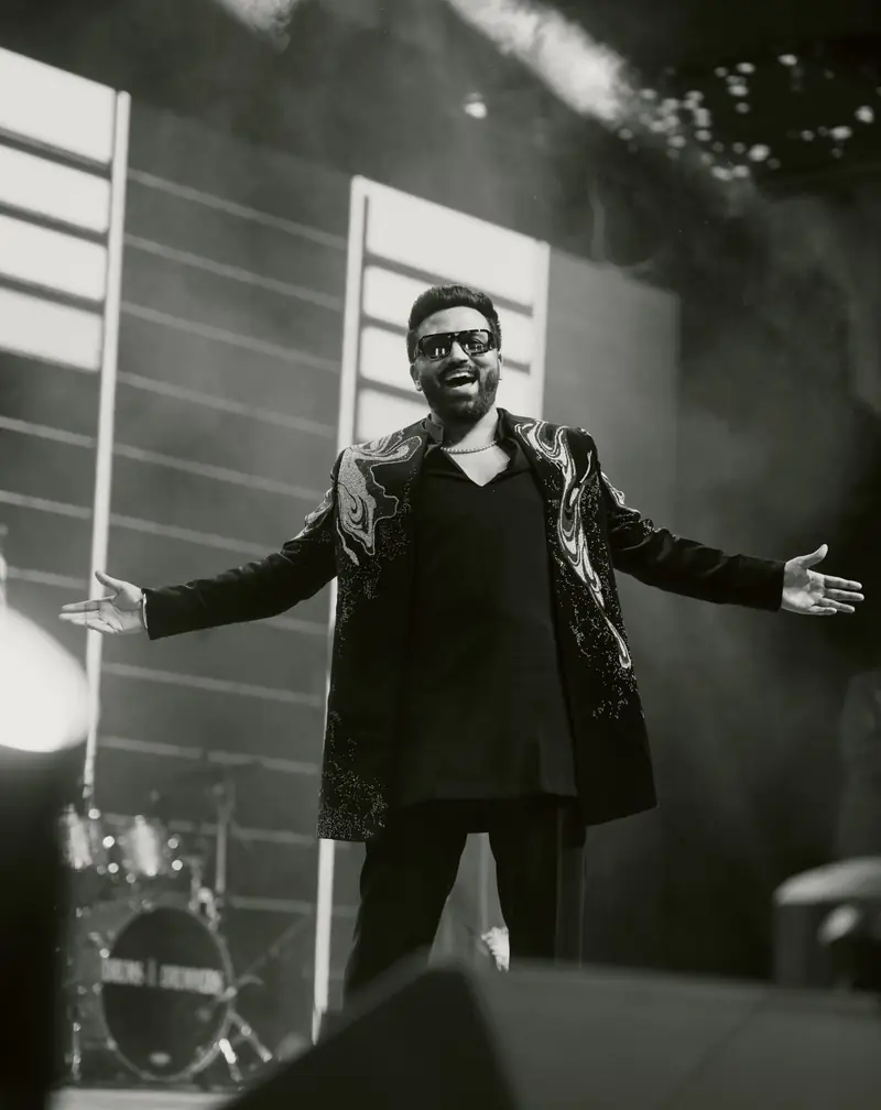 Black and white photo of the groom on stage with his arms flung wide