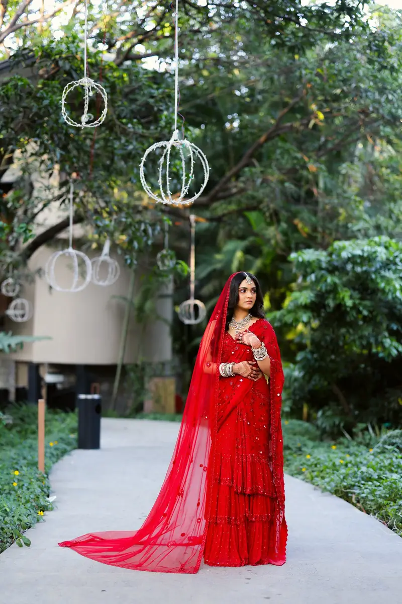The bride standing on a garden path with her long red dupatta trailing behind her