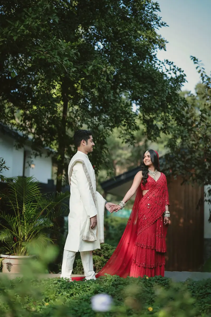 The couple holding hands across a green garden on their wedding day