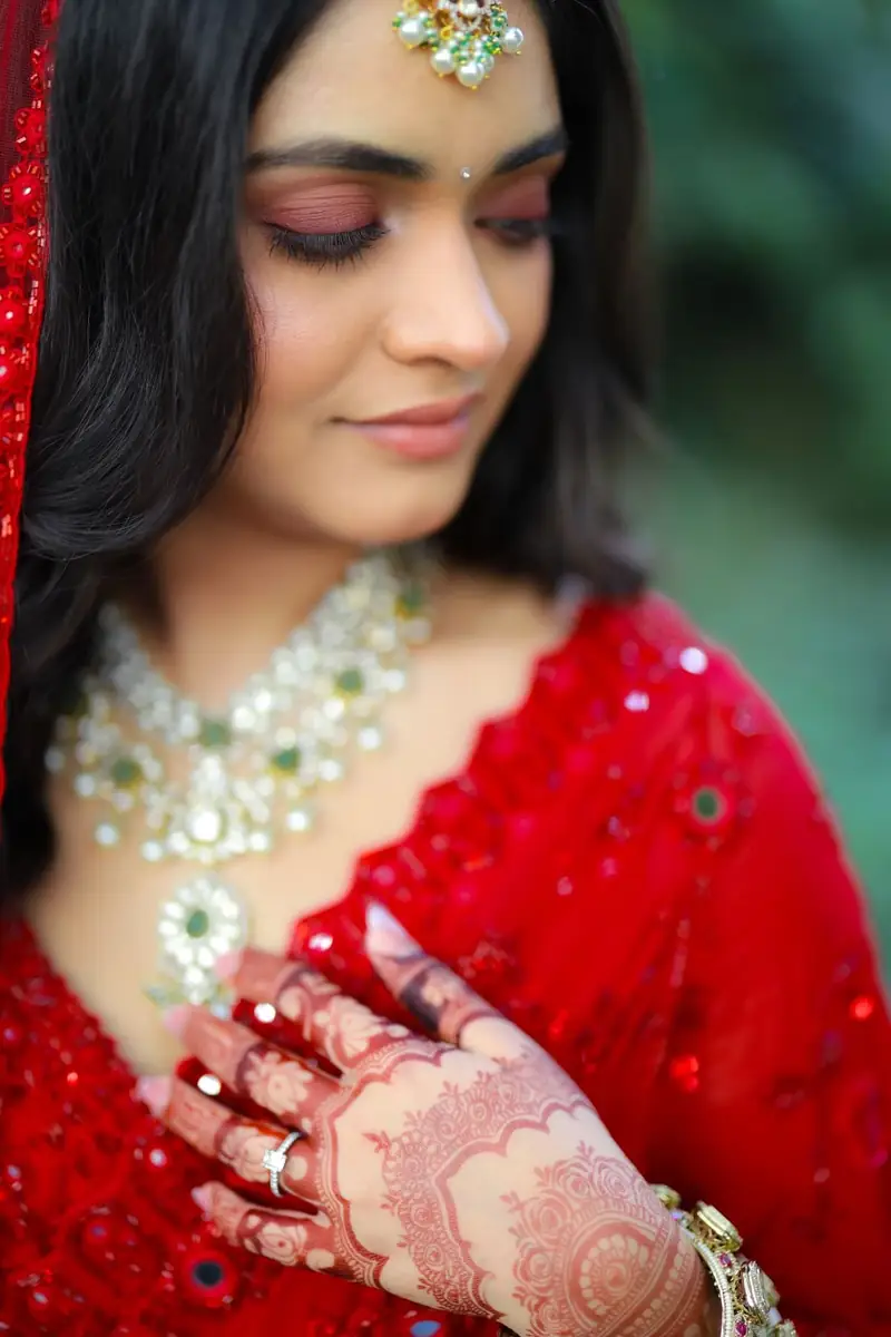 A bride in a red lehenga and kundan necklace looking down at her mehendi